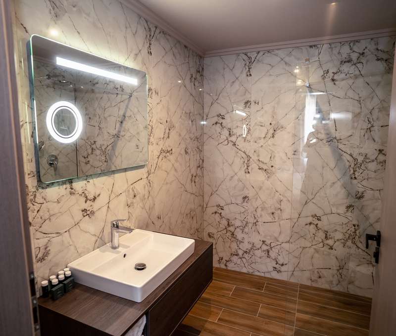 Kúpeľňa má elegantný dizajn so keramickými dlaždicami a vlastnými umývadlami a LED zrkadlom.